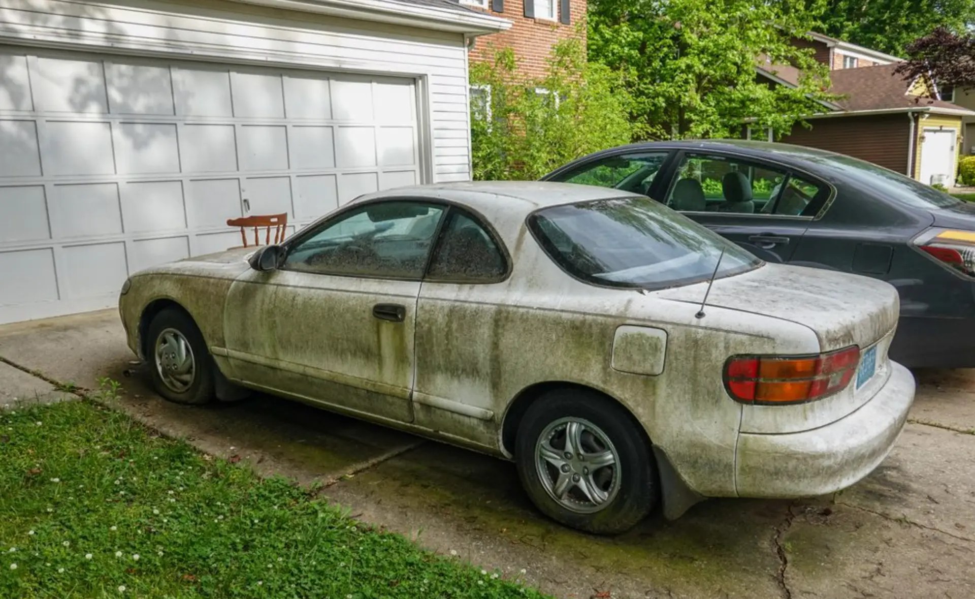 A weathered, moss-covered coupe that has been sitting unused in a driveway